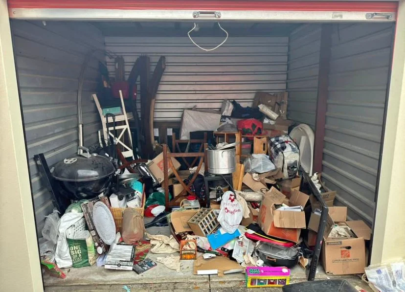 A cluttered storage unit filled with assorted household items, furniture, boxes, and miscellaneous objects.