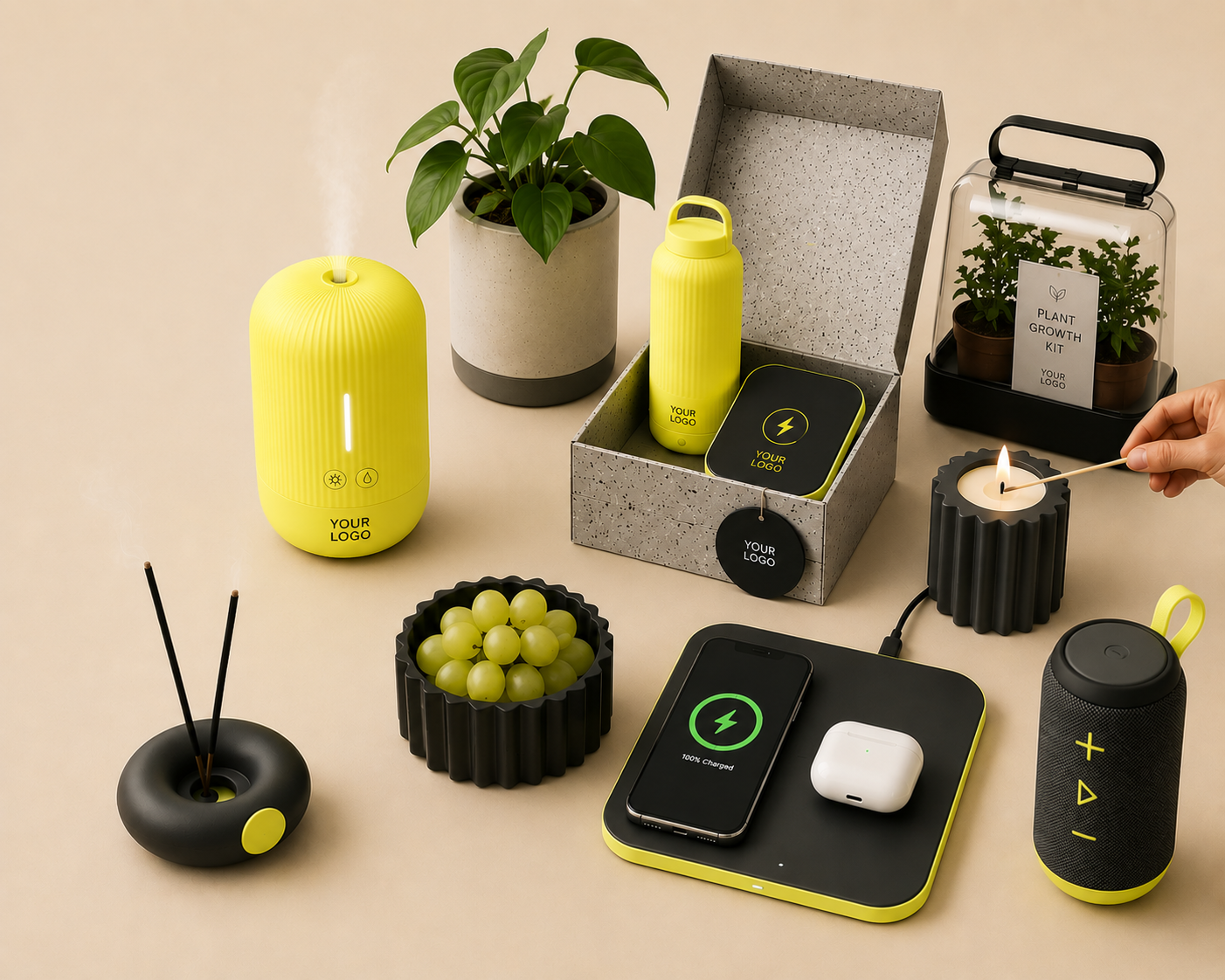 A collection of modern tech gadgets, a potted plant, and some gardening items on a beige surface. The gadgets include a yellow diffuser, a yellow water bottle, a black portable speaker, a phone charging on a wireless pad, a black incense holder, and a black candle with a person lighting it with a match. There is also a black container filled with green grapes and a plant growth kit in the background.