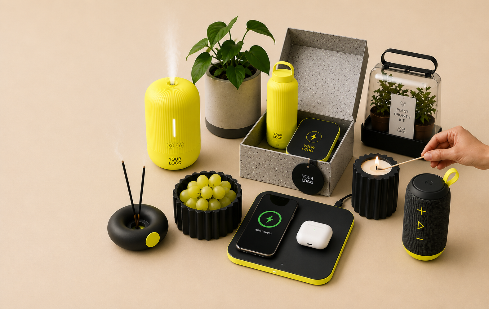 A collection of modern home and office accessories including a yellow humidifier, potted plant, water bottle, black and yellow wireless charger, small black diffuser, bowl of green grapes, smartphone charging, wireless earbuds, scented candles, a black portable speaker, and a plant growth kit, all arranged on a beige surface.
