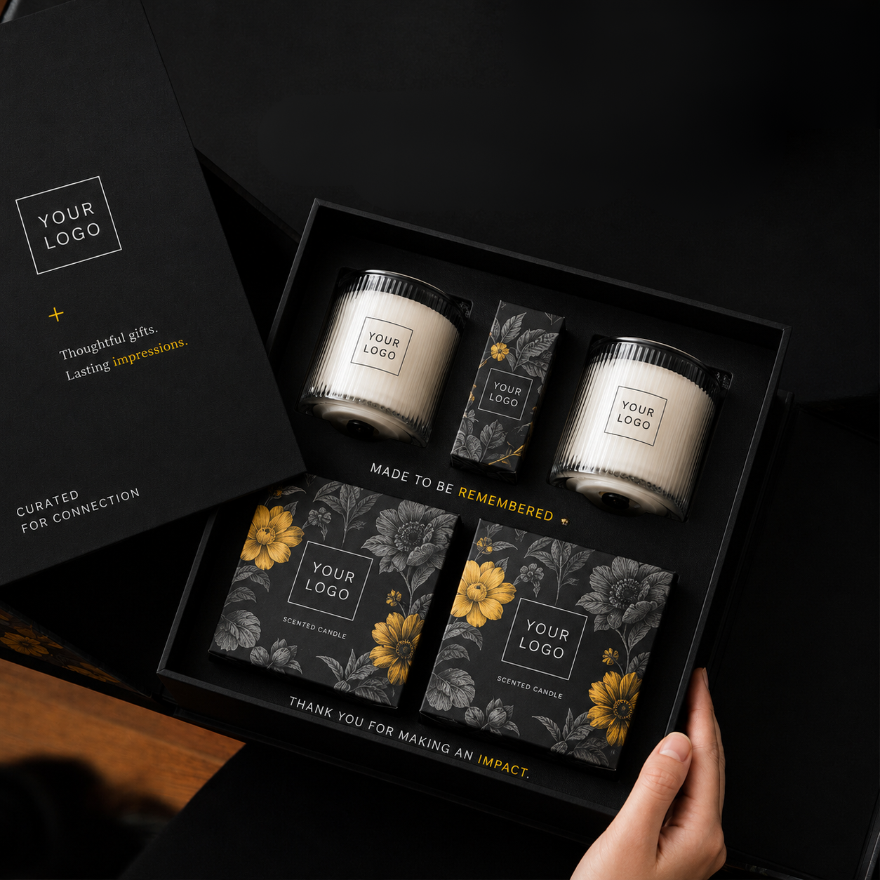 Gift box containing two scented candles, a small box, and two boxed scented candles, all with black and yellow floral designs, arranged in a black box with a card.