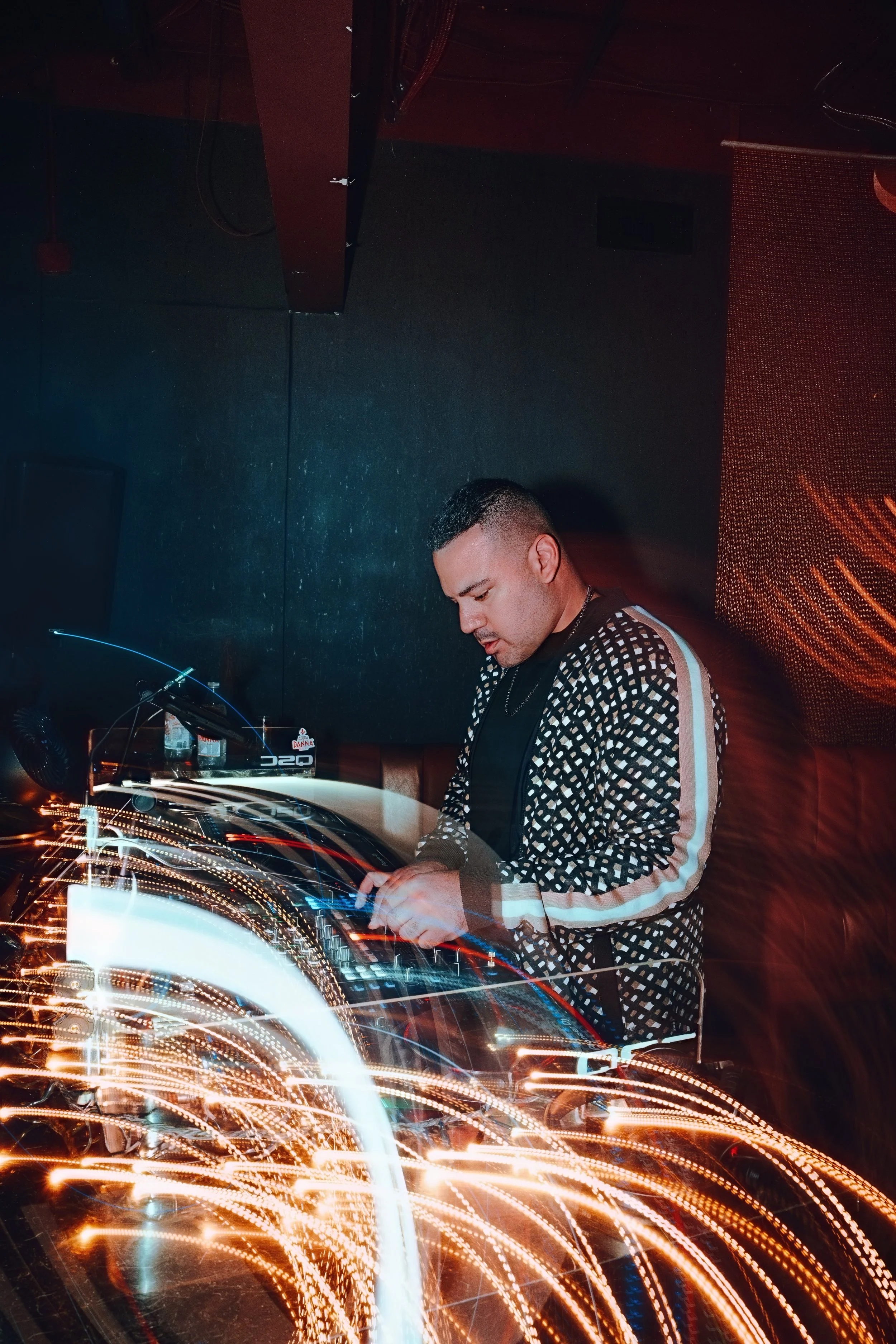 A DJ performing in a dark club with colorful light streaks and a digital screen background.