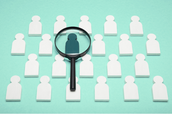 Magnifying glass over dark green person icon amongst rows of white person icons. Teal background. Investigation case study
