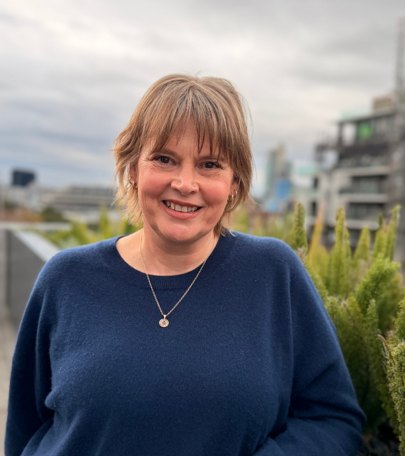 Woman wearing necklace smiling, outdoor urban setting.