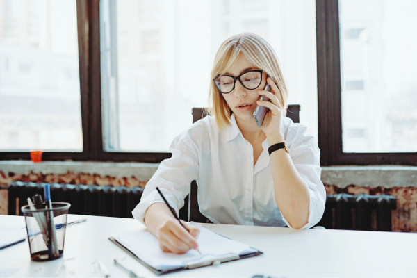 professional female with glasses on phone at desk taking notes