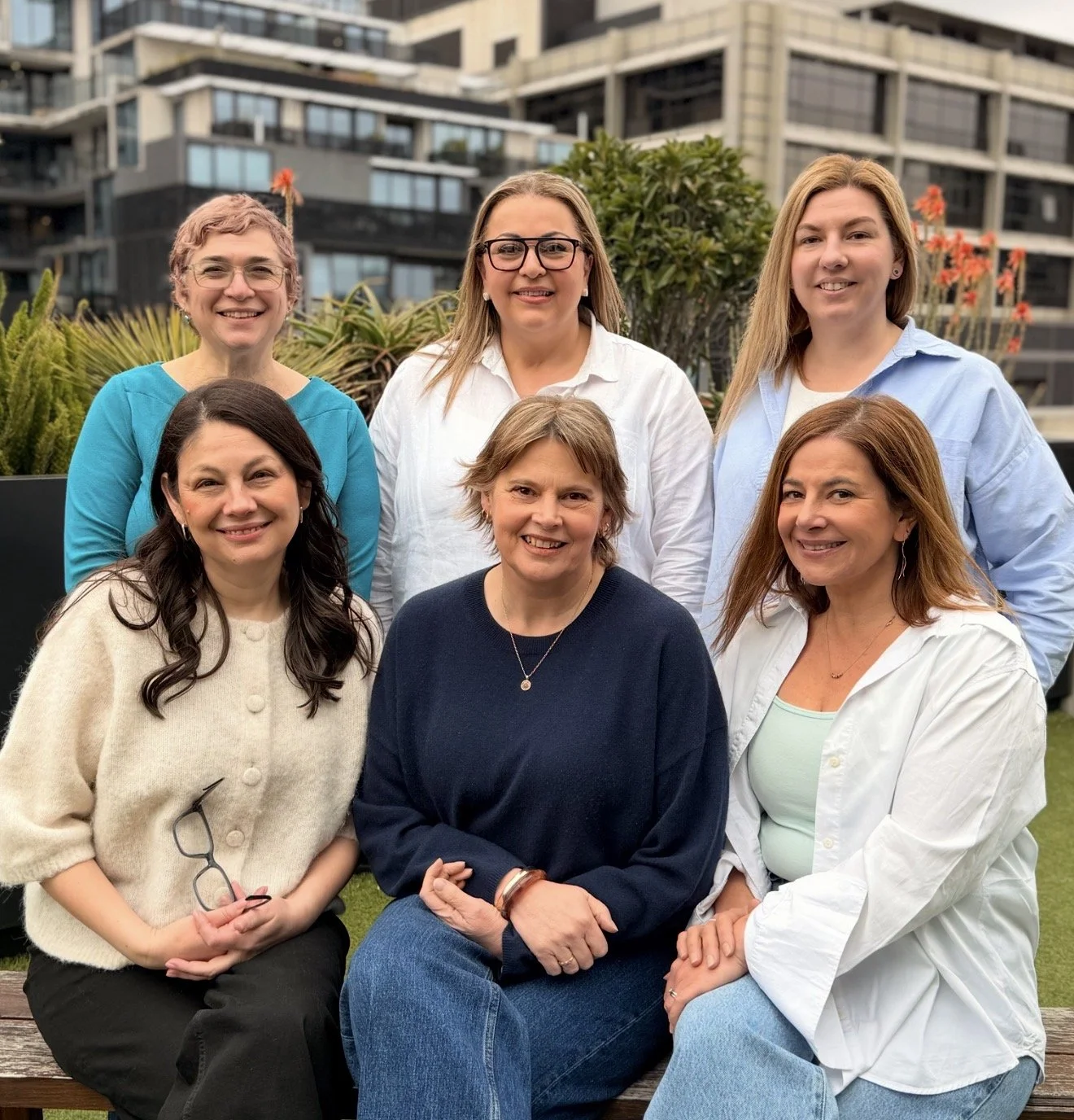 Six professional women smiling in an urban outdoor setting.