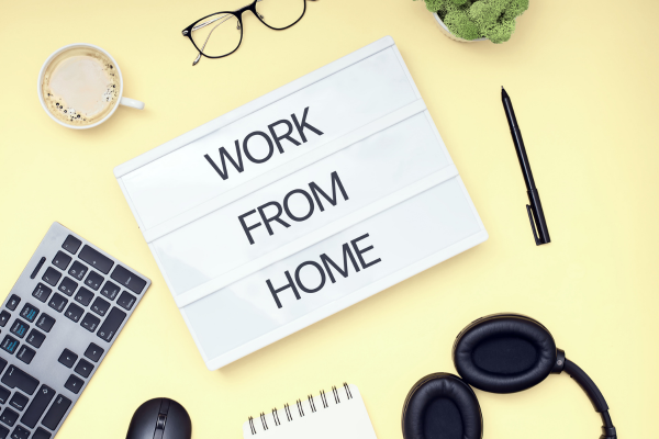 Work From Home sign on yellow desktop with glasses, coffee, headphnes, keyboard, pen, plant, notebook