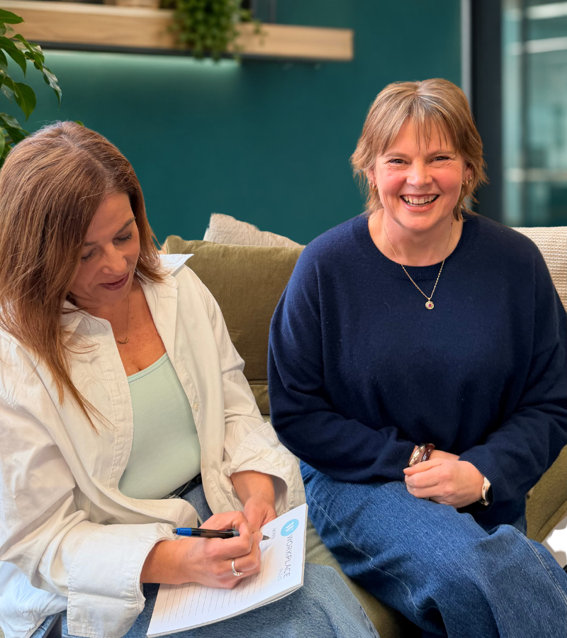 two professional women, one writing on notepad, the other smiling