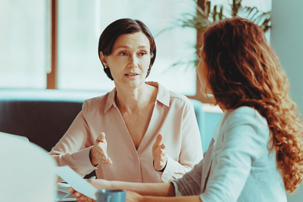Two seated colleagues in office setting. Manager explaining something to team member using hand gesture.