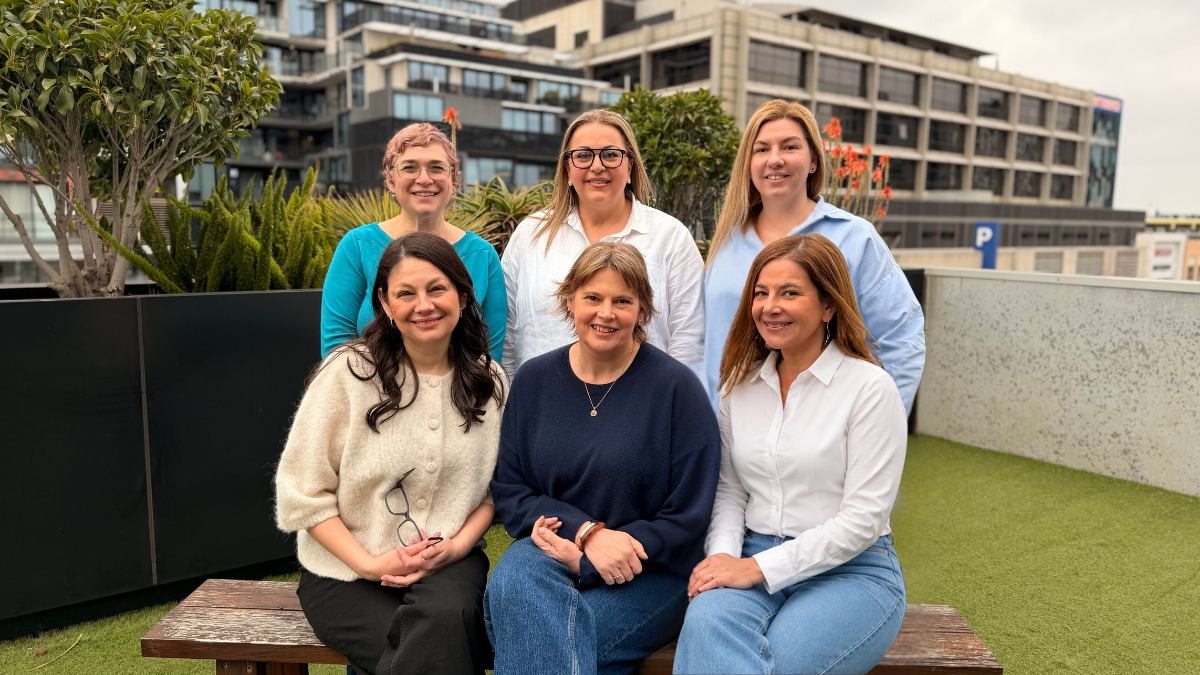 Six professional women smiling in an urban outdoor setting.