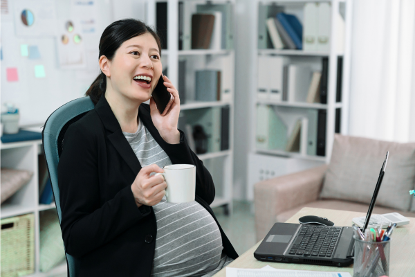 Pregnant worker on phone at desk, smiling and holding mug