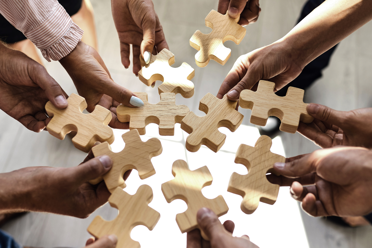 Multiple hands holding and connecting wooden puzzle pieces in a circular arrangement.