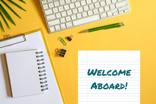 yellow desk scene. notepad, keyboard, pen, etc. "Welcome Aboard!"