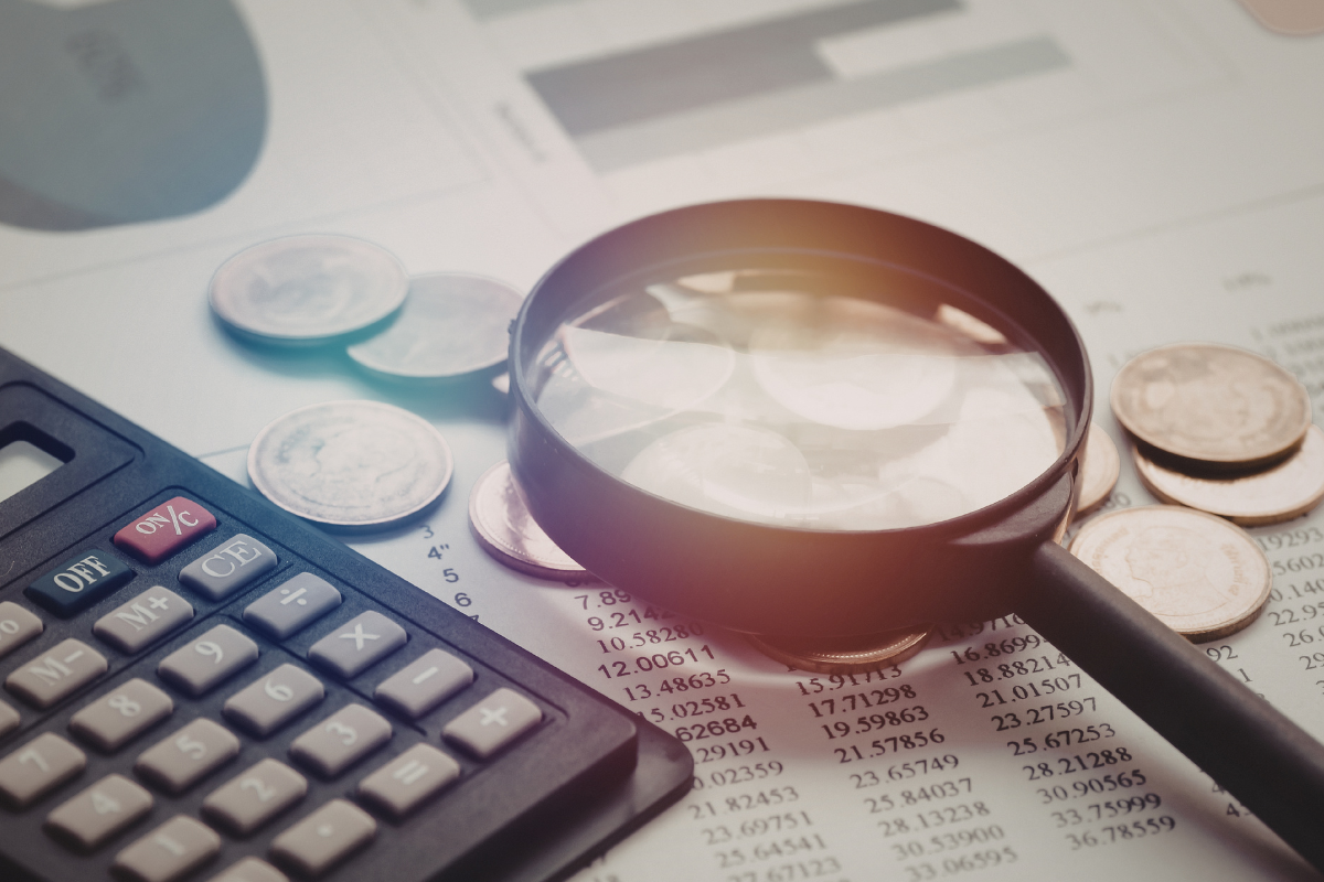 Close-up of financial records with coins, a calculator, and a magnifying glass placed on top of the documents.