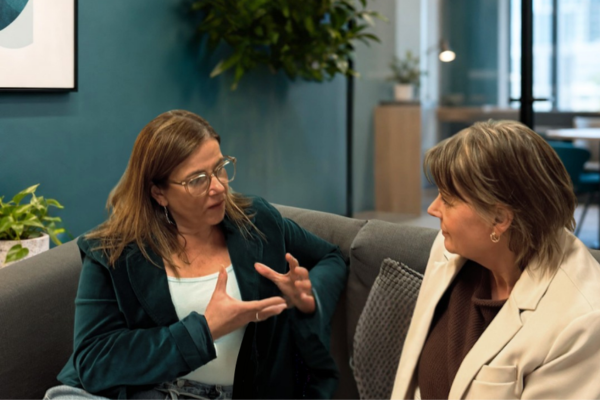 Two profressional women engaged in courageous conversation on couch. Teal office setting.