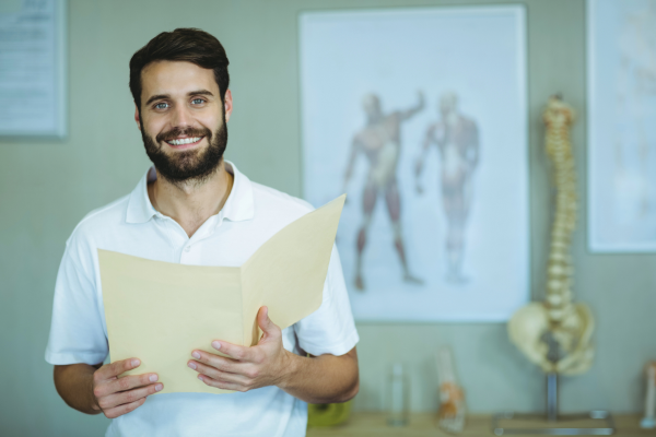 Allied health professional holding open manila folder. anatomy poster and model in background.