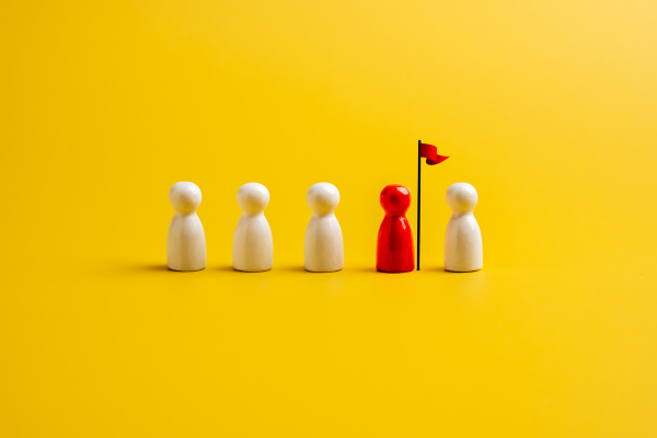 yellow backgrond. five people pieces, four are white, one is red. the red pirce has a red flag.