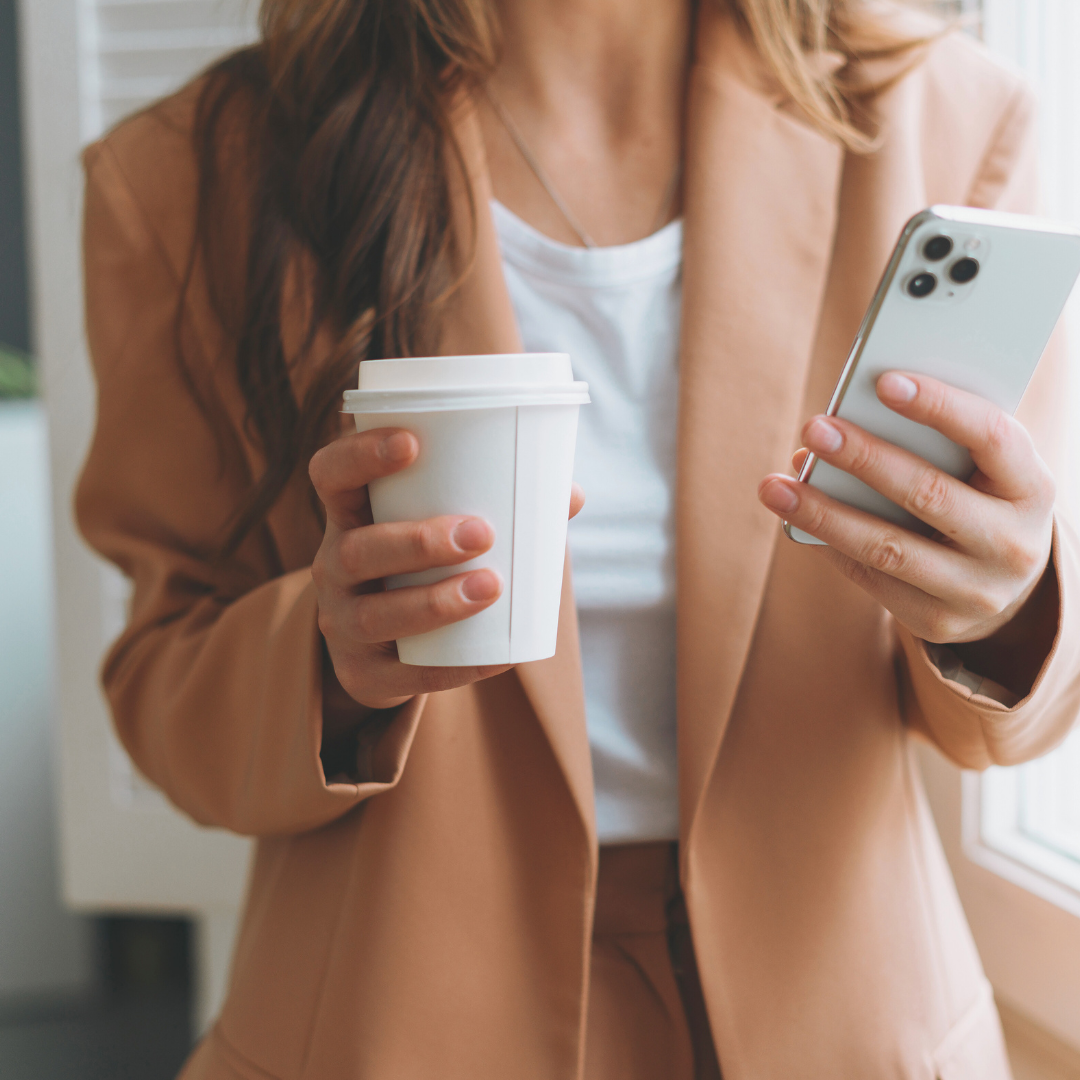 Busy woman holding a cup of coffee and scrolling on her mobile phone