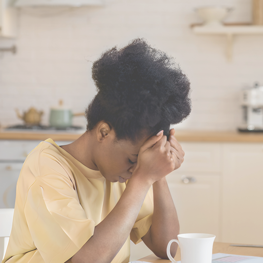 Overwhelmed woman in kitchen, sat with cup of tea and head in her hands