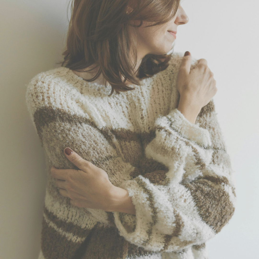 Woman in cosy brown jumper hugging herself