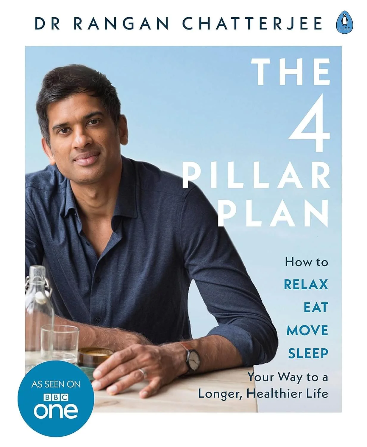 Book cover titled 'The 4 Pillar Plan' by Dr. Rangan Chatterjee, featuring a man with short dark hair wearing a navy blue shirt, sitting at a table with a glass of water and a bottle, against a light blue background.