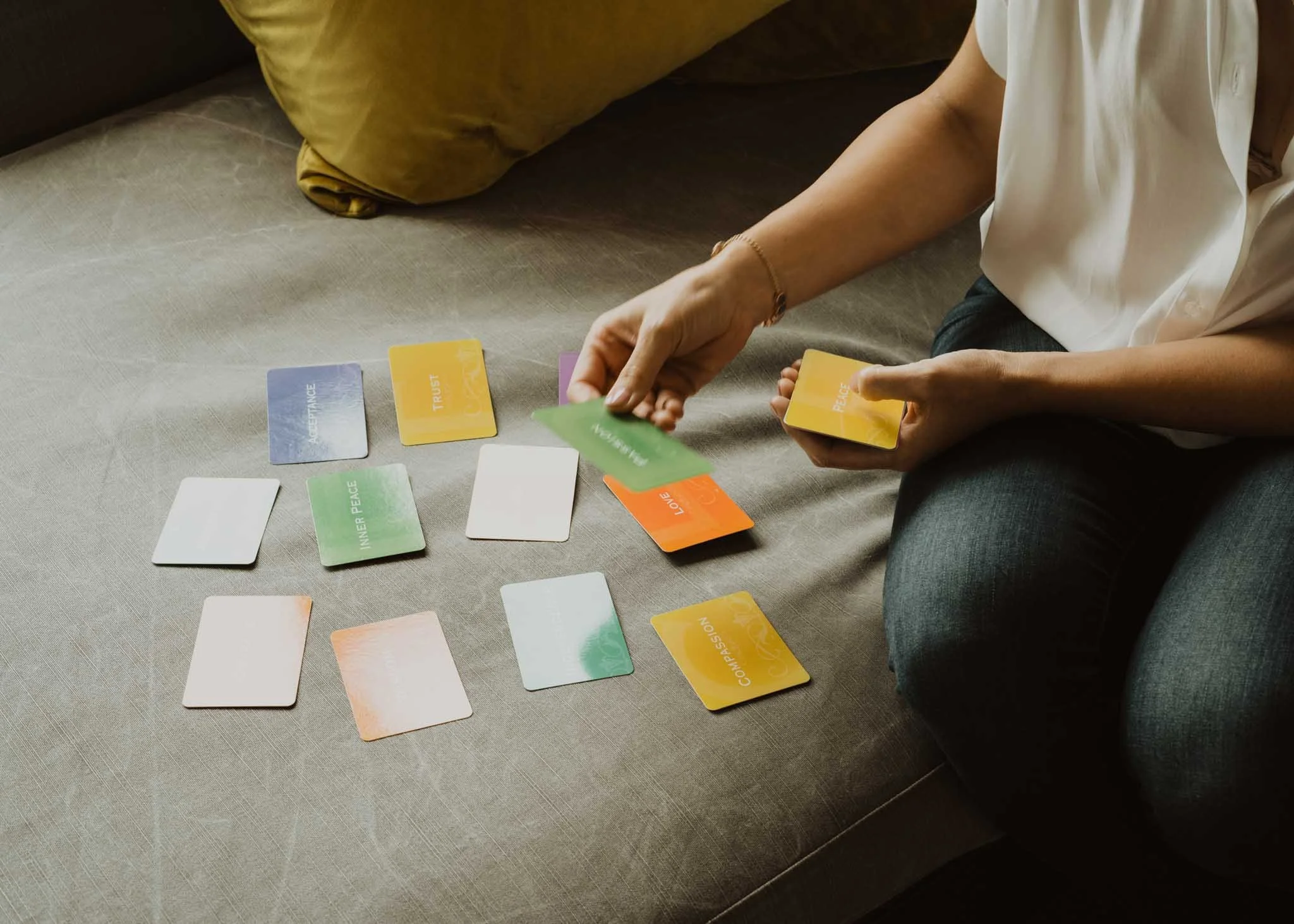 Person sitting on a couch playing a card game with colorful cards spread out on a table.
