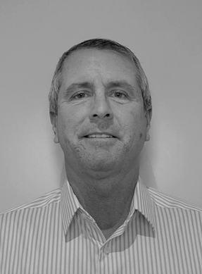 Black and white portrait of a middle-aged man with short hair, wearing a collared shirt, smiling against a plain background.