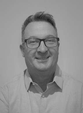 Black and white photo of a man smiling, wearing glasses and a collared shirt.