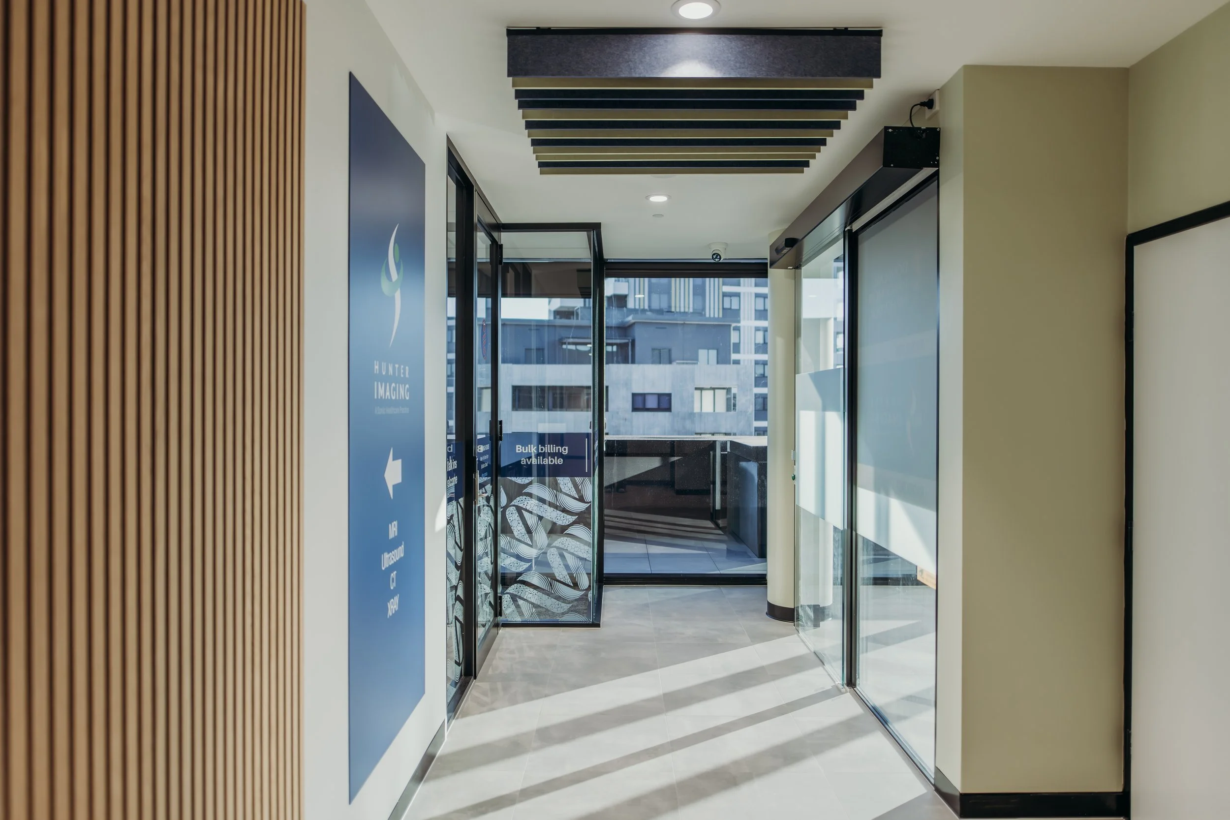 Interior view of a modern building entrance with glass doors, wooden wall paneling, and a blue sign with an arrow and text indicating directions.