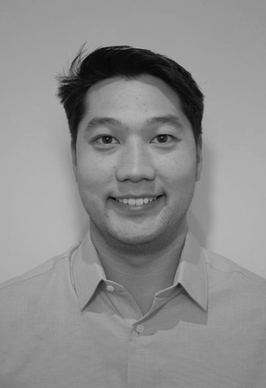 A black and white portrait of a smiling young man with short dark hair, wearing a collared shirt.