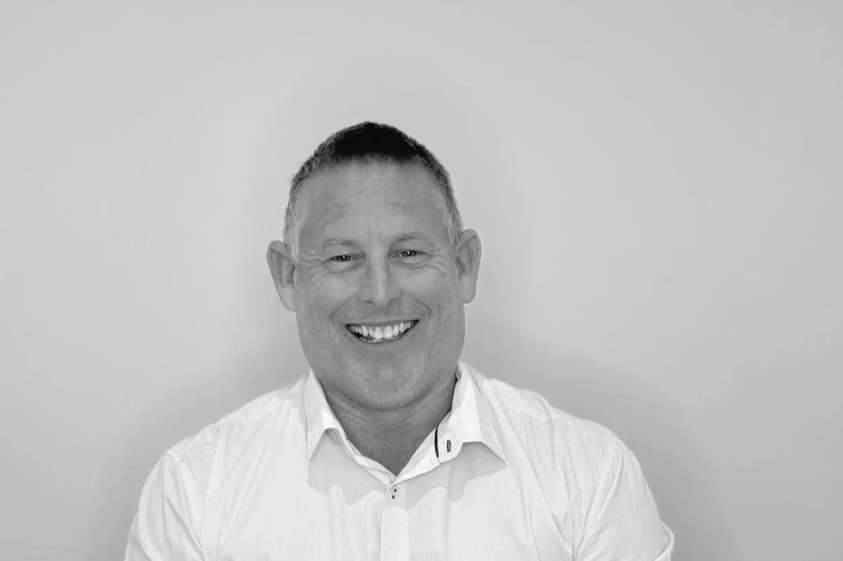 A smiling man with short hair wearing a white button-up shirt.