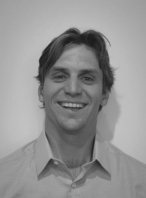 A black and white photo of a smiling young man with medium-length hair, wearing a collared shirt.