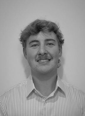 A young man with curly hair and a mustache, wearing a striped collared shirt, smiling at the camera, against a plain background.