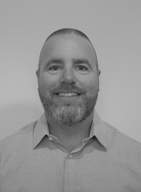 Portrait of a smiling man with short hair and a beard, wearing a collared shirt, against a plain background.