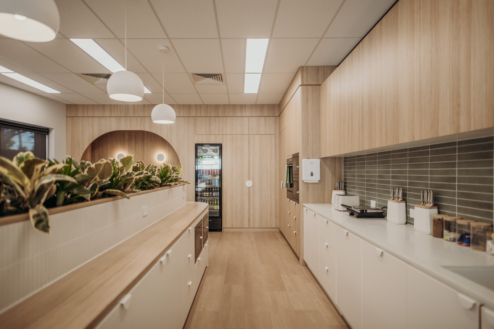 Modern kitchen with light wood cabinets, white countertops, gray tile backsplash, and pendant lights.