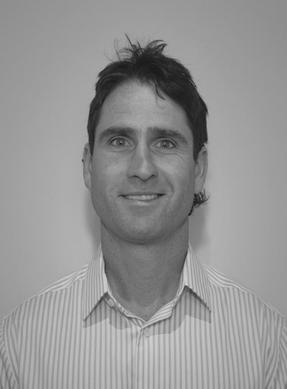Black and white photo of a man with dark hair wearing a striped collared shirt, smiling at the camera against a plain background.