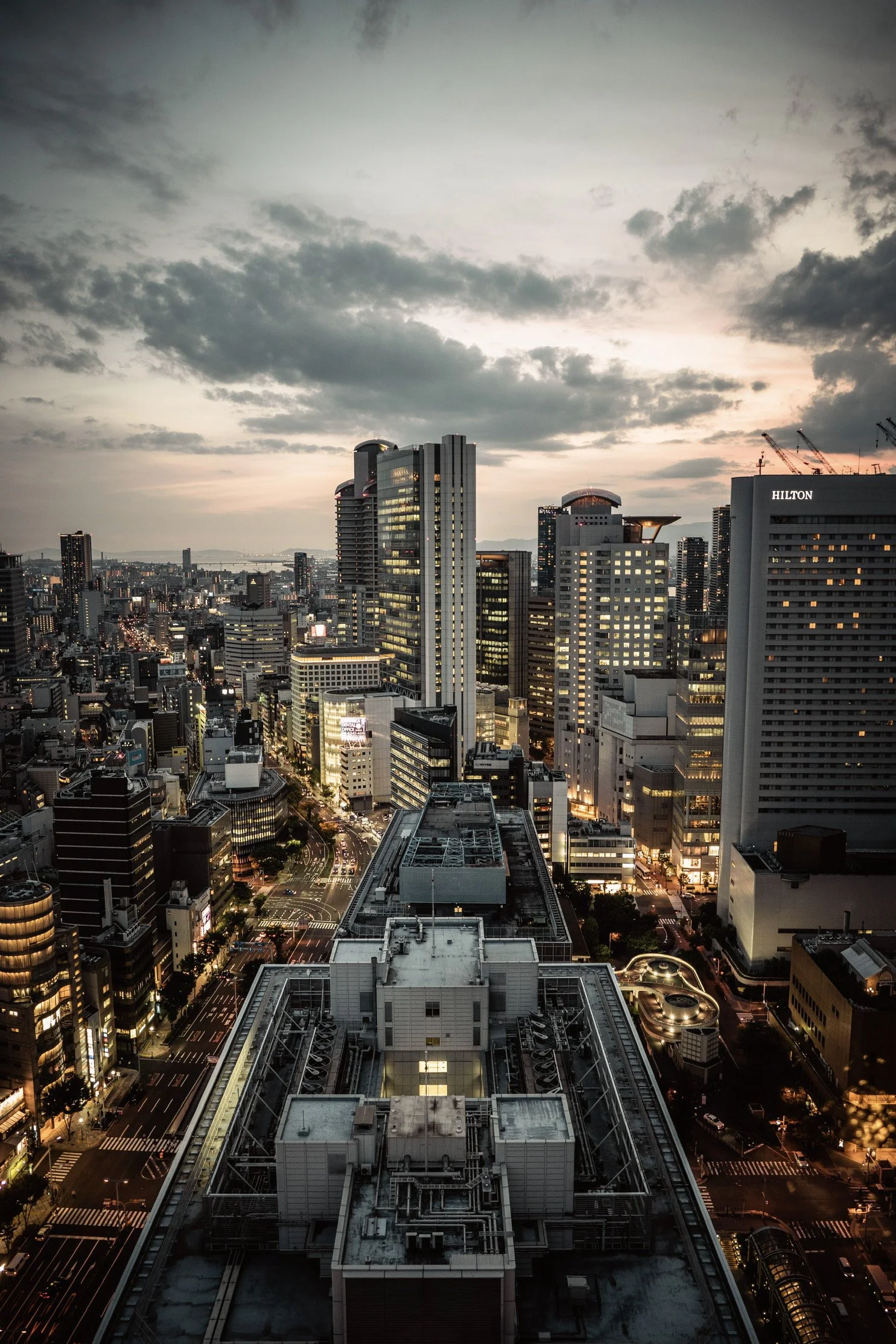 高層ビルが立ち並ぶ都市の夜景、曇り空と夕焼けの空模様。