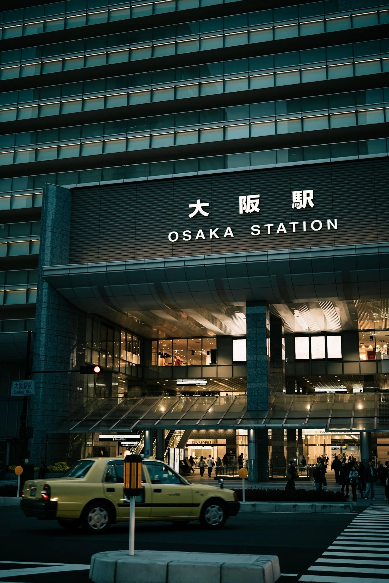 大阪駅前にある高層ビルの外観と交差点を通る車や歩行者の風景。