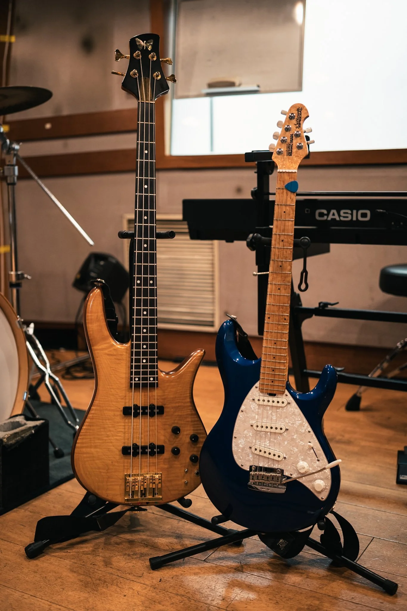 木製の電気ベースと青いエレキギターが並んで立てられている音楽スタジオの室内風景。