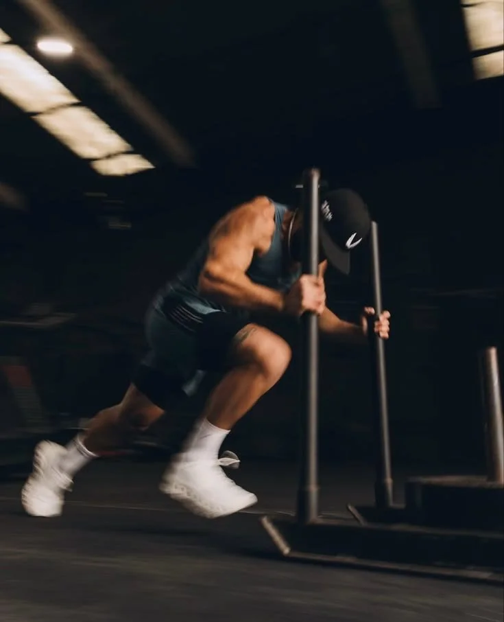 Athletic man in a cap pushing a weighted sled during an intense gym workout