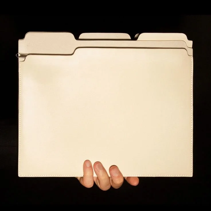 A hand holding a beige file folder or binder with three tabbed dividers inside, against a black background.