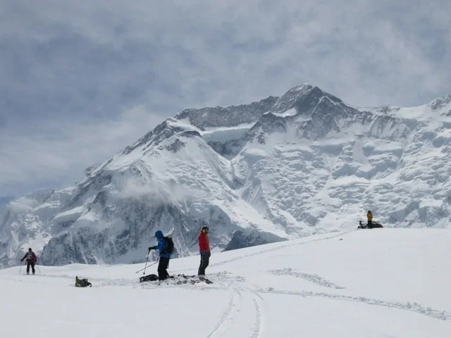 People skiing and snowboarding in a snowy mountain landscape with cloudy sky.