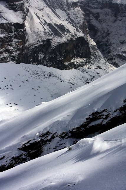 Snow-covered mountain landscape with steep slopes and rocky cliffs in the background.