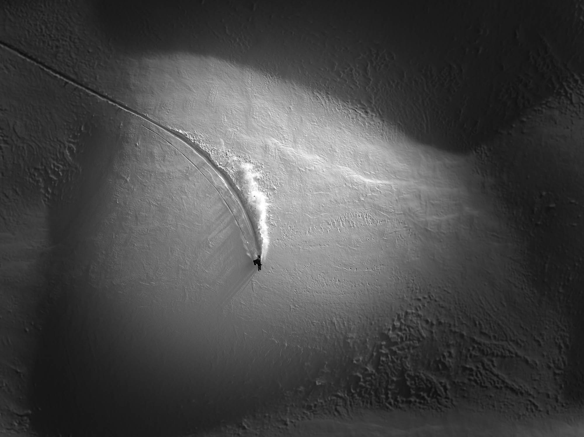 A person skiing down a snow-covered slope at night, illuminated by a beam of light, with ski tracks visible on the snow.