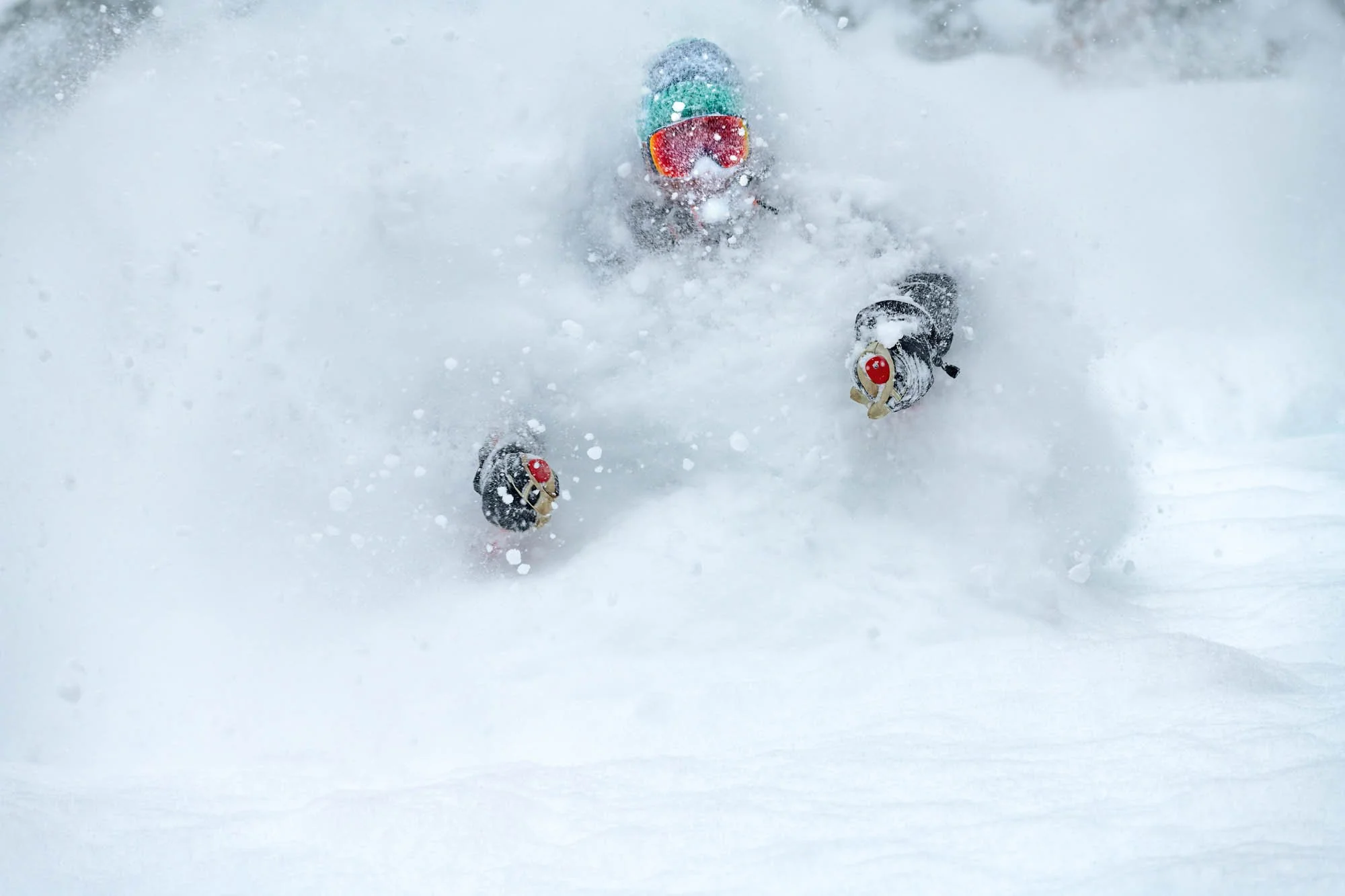 A person skiing or snowboarding in the snow, wearing goggles and winter gear, with snow flying around them.
