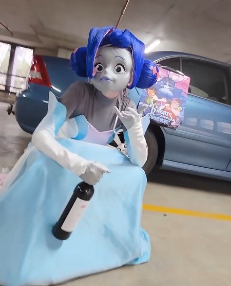 Person dressed as a cartoon character with large blue hair and a gray face sitting in a parking garage, holding a water bottle with a cartoon movie poster in the background.