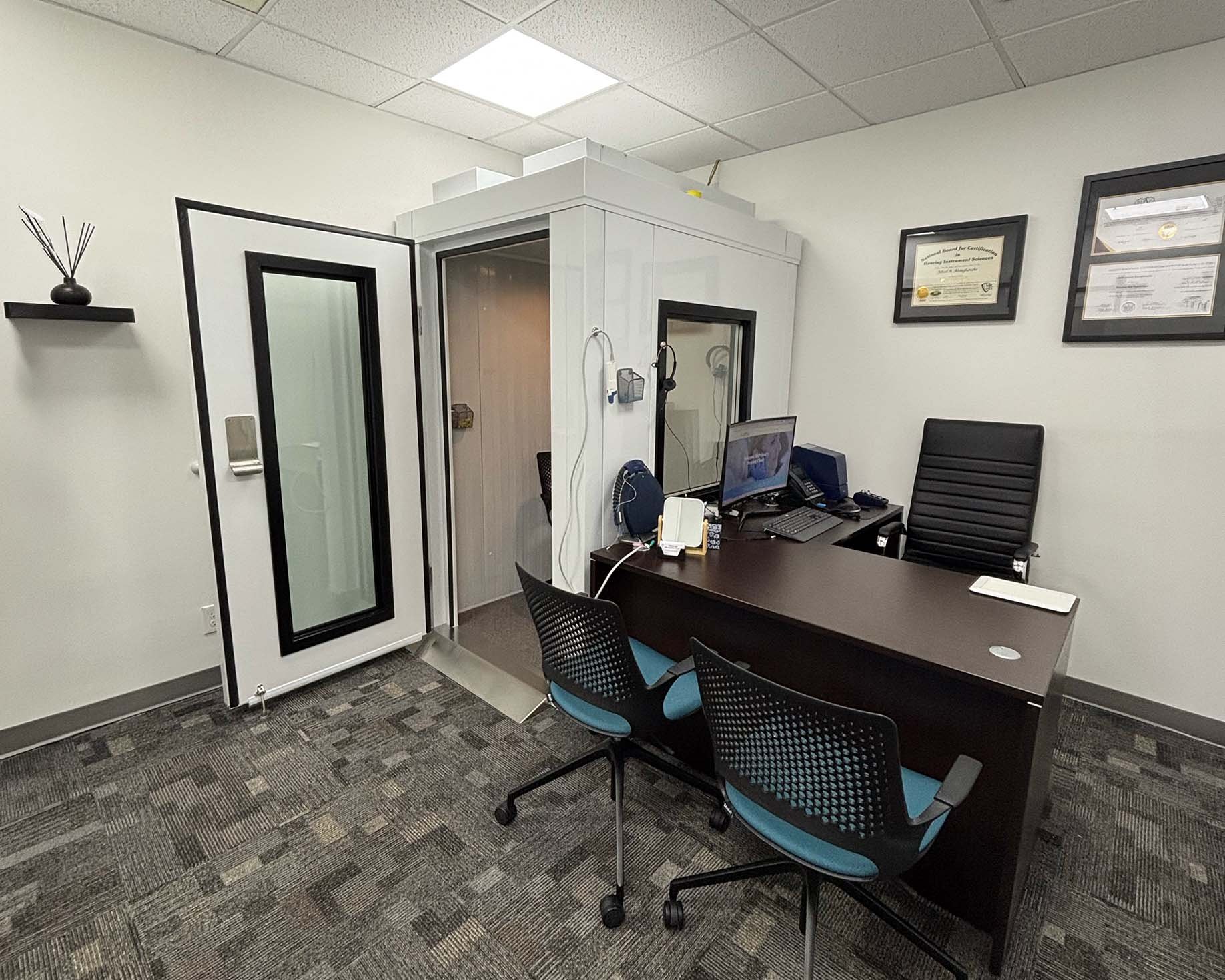 A small office with a desk, computer, and chairs, with framed diplomas on the wall.