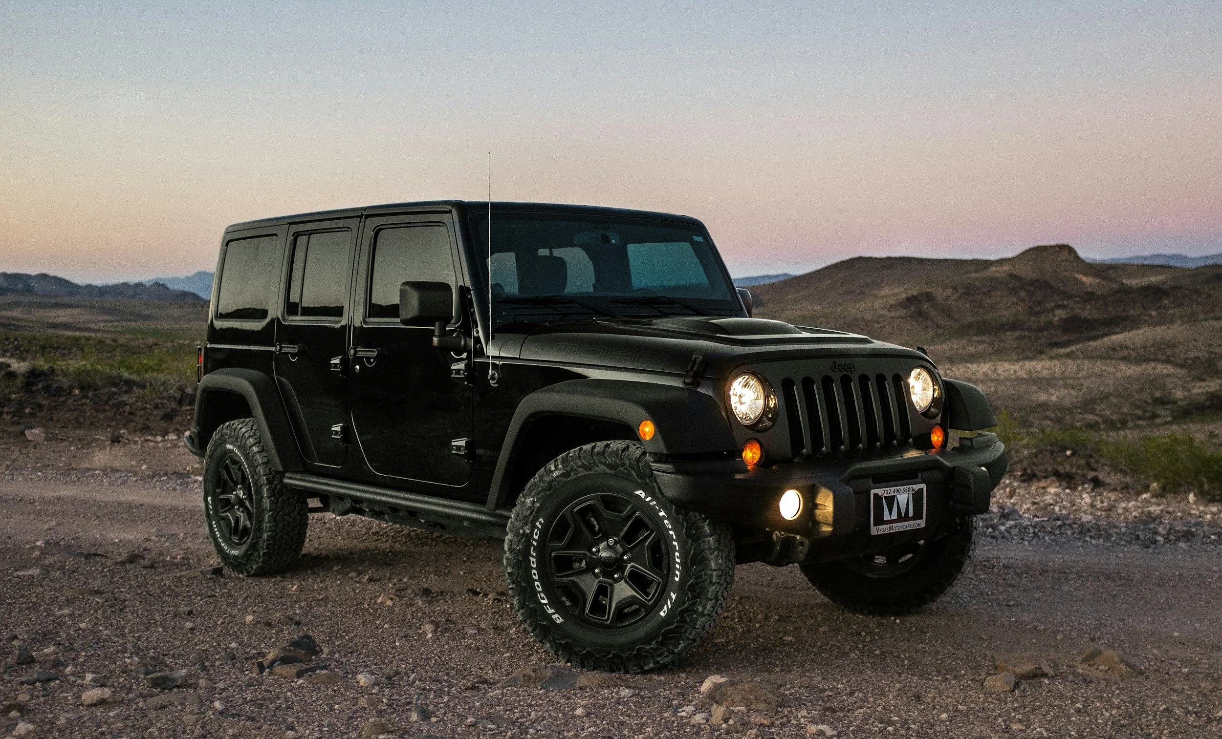 Black Jeep SUV parked on a dirt road in a desert landscape during dusk.
