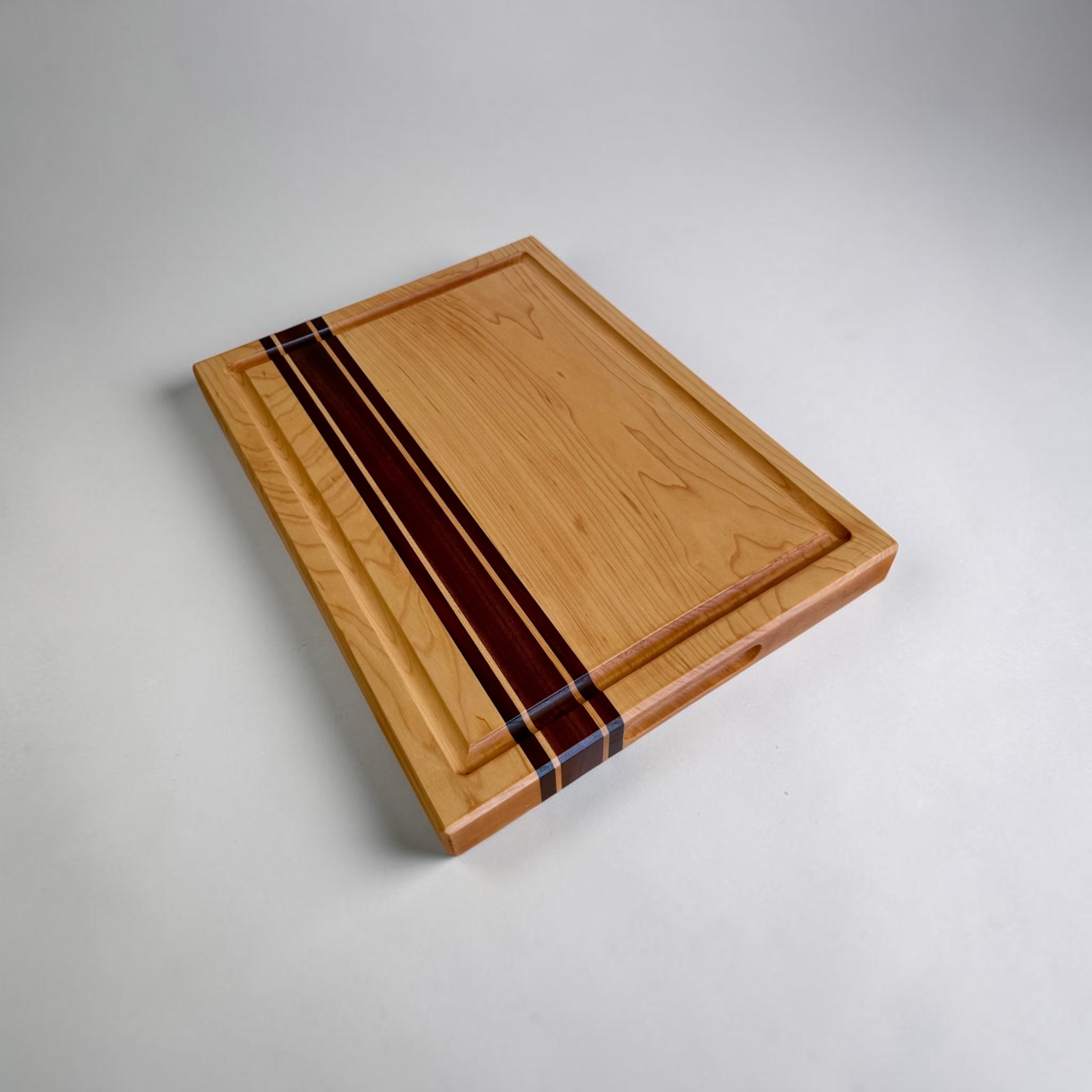 Maple cutting board with sapele and padauk accent stripes and juice groove, angled view
