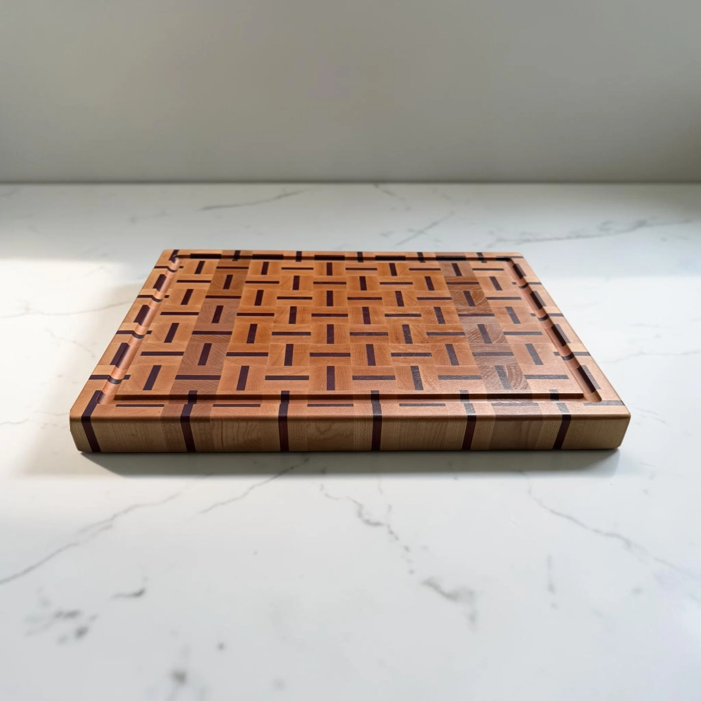 A one-of-a-kind end-grain cutting board in maple and bloodwood, 1.5" thick with side handles and a juice groove. Handmade in Philadelphia, ready to ship