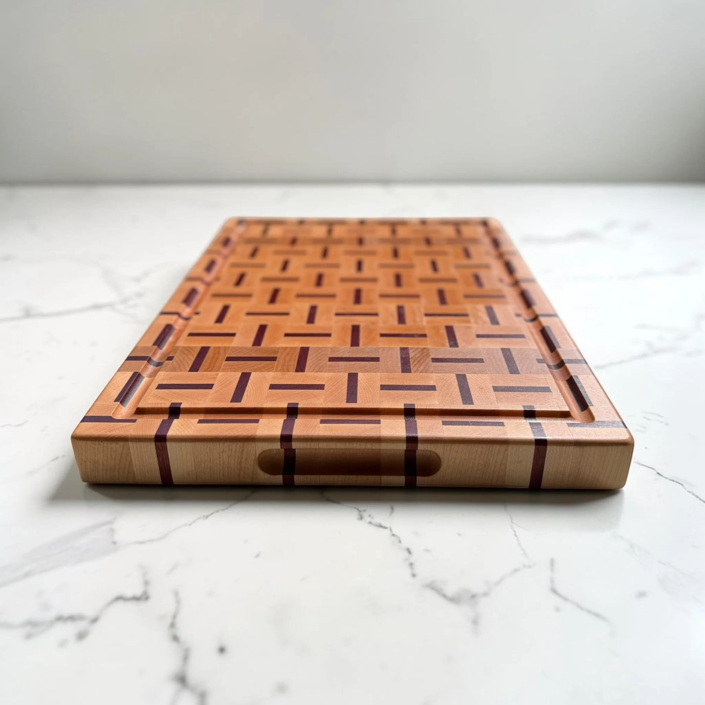 A one-of-a-kind end-grain cutting board in maple and bloodwood, 1.5" thick with side handles and a juice groove. Handmade in Philadelphia, ready to ship